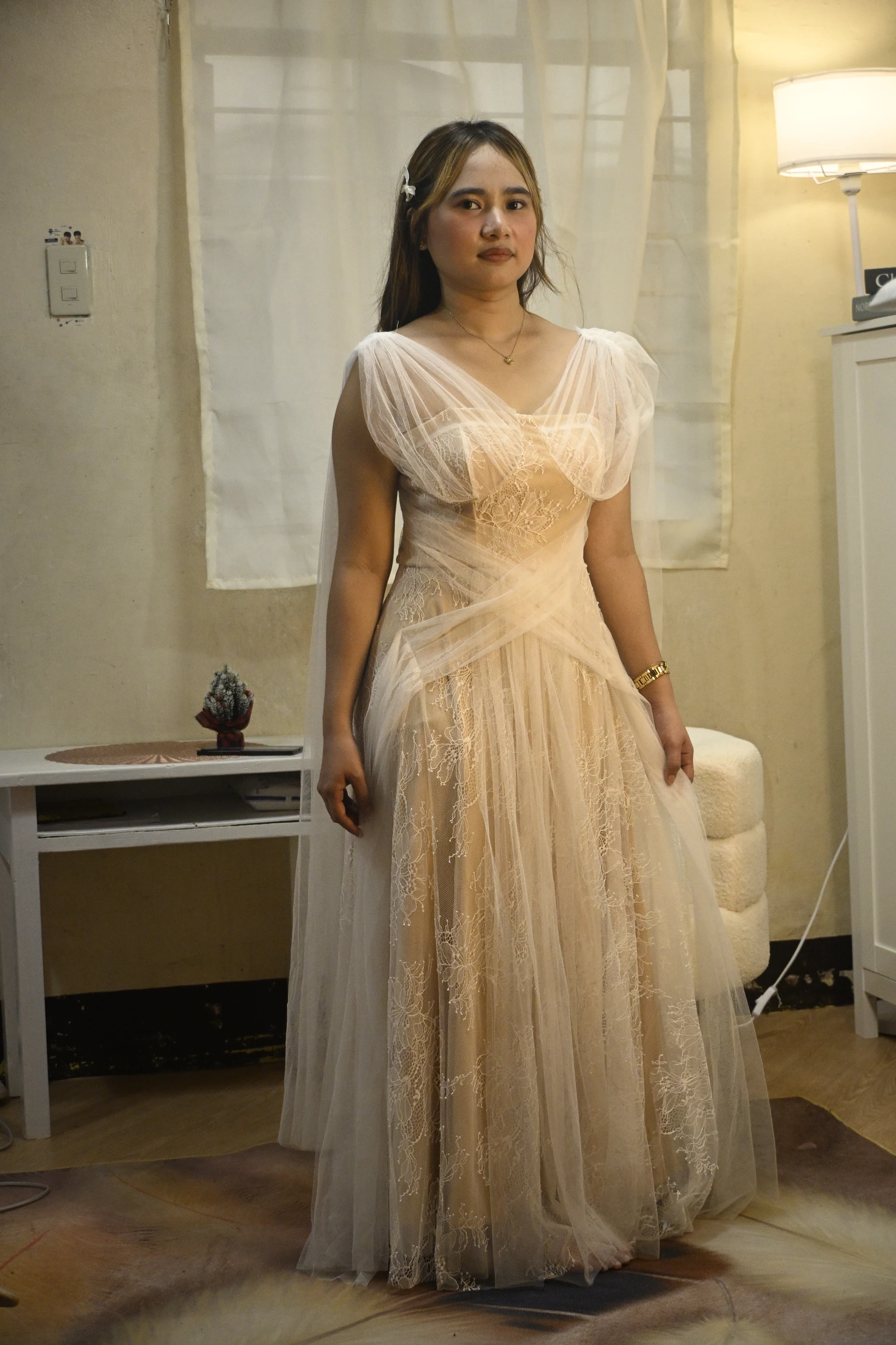 Model wearing a cream lace gown with draped tulle across the shoulders and waist.