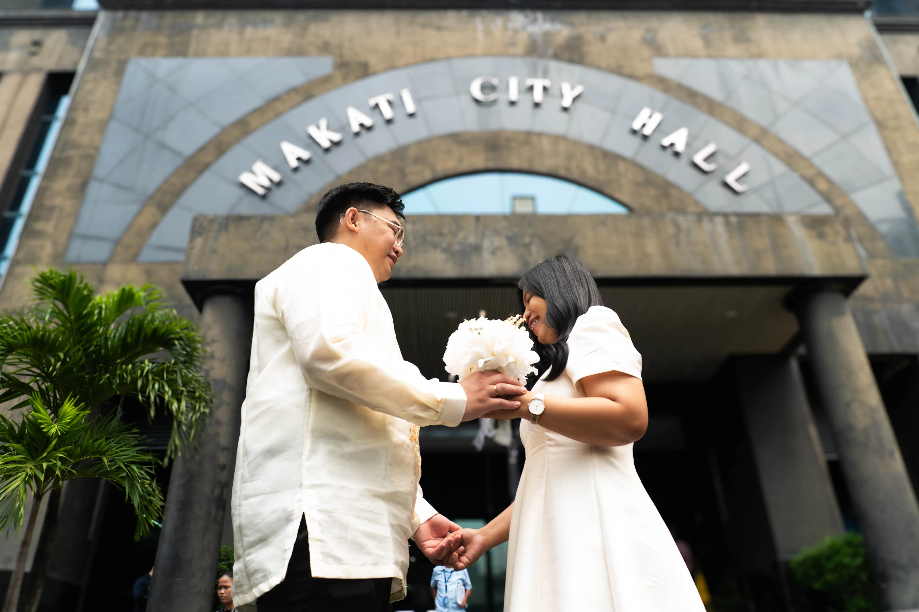 The couple holds hands beneath the Makati City Hall entrance sign.