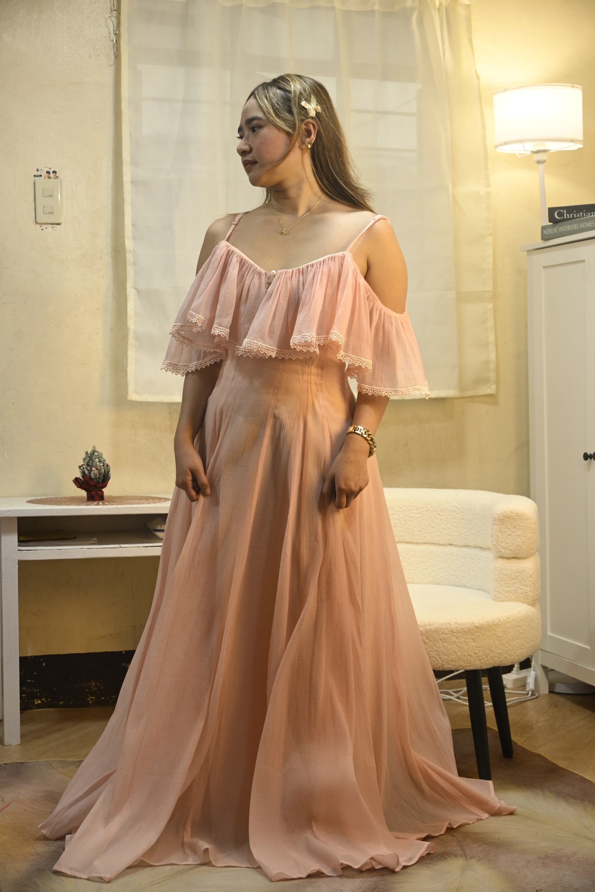 Full-length view of a blush chiffon gown with shoulder cutouts, tiered neckline ruffles and a flowing skirt.