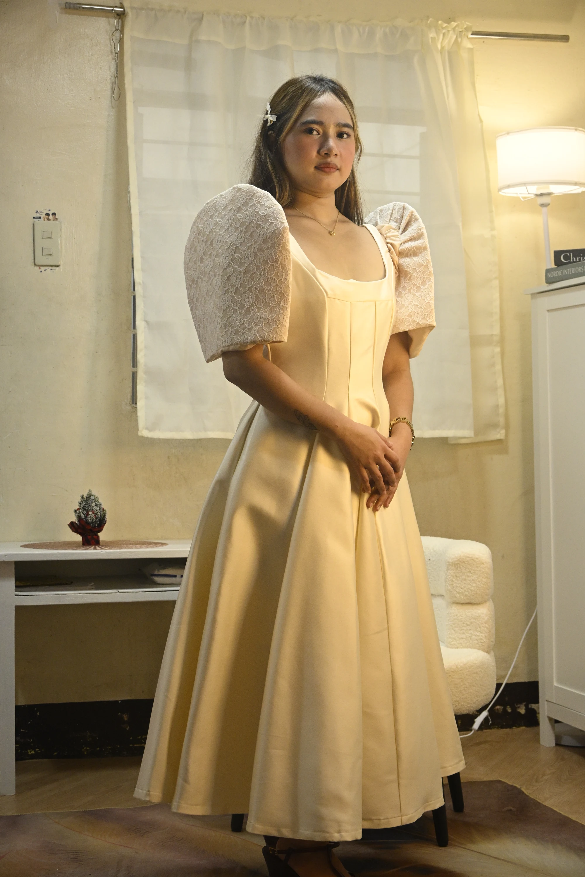 Model in a champagne-colored long dress with lace puff sleeves and a pleated skirt, photographed indoors.