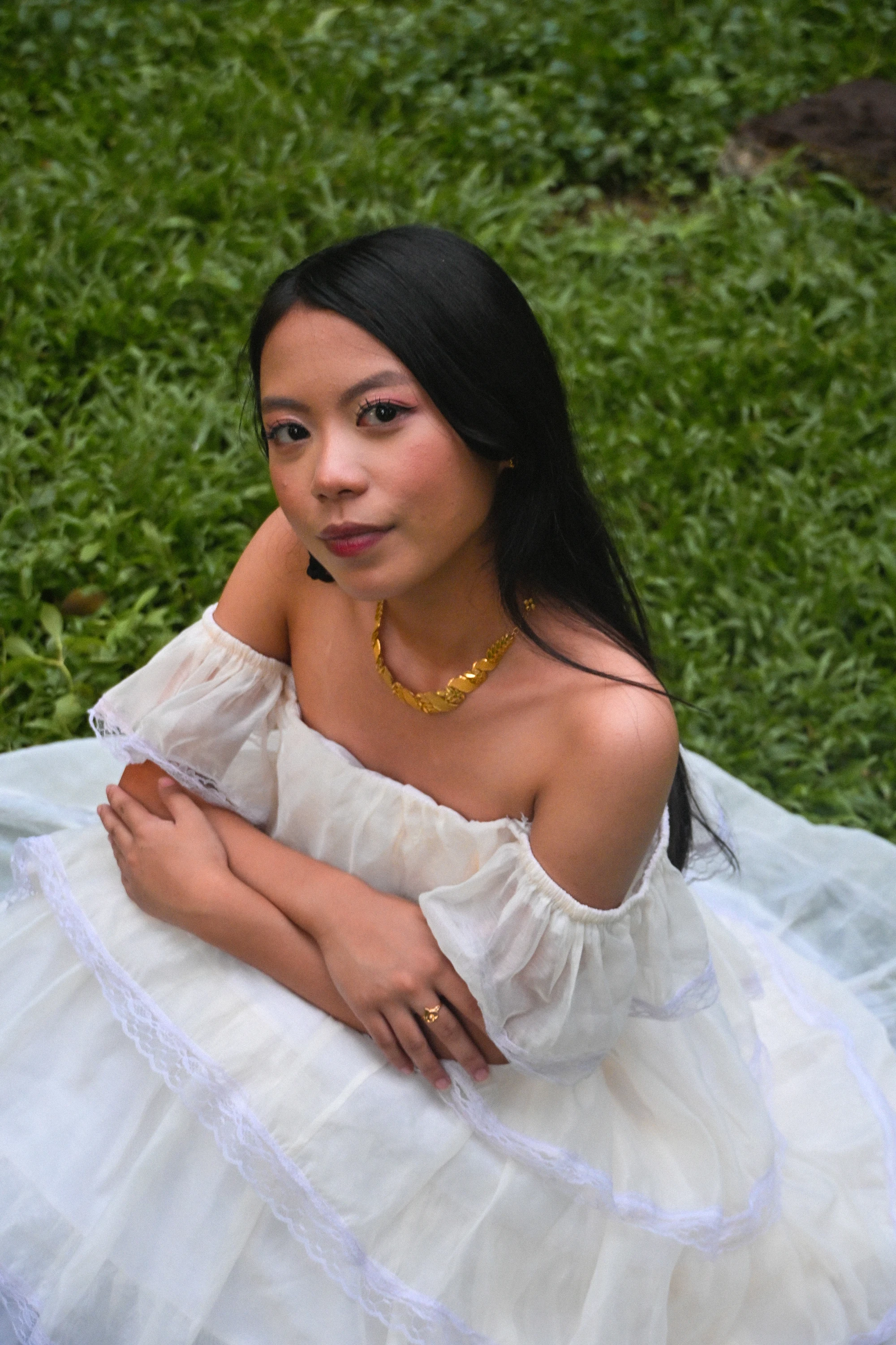 Seated portrait in a white gown, looking toward the camera on a garden lawn.