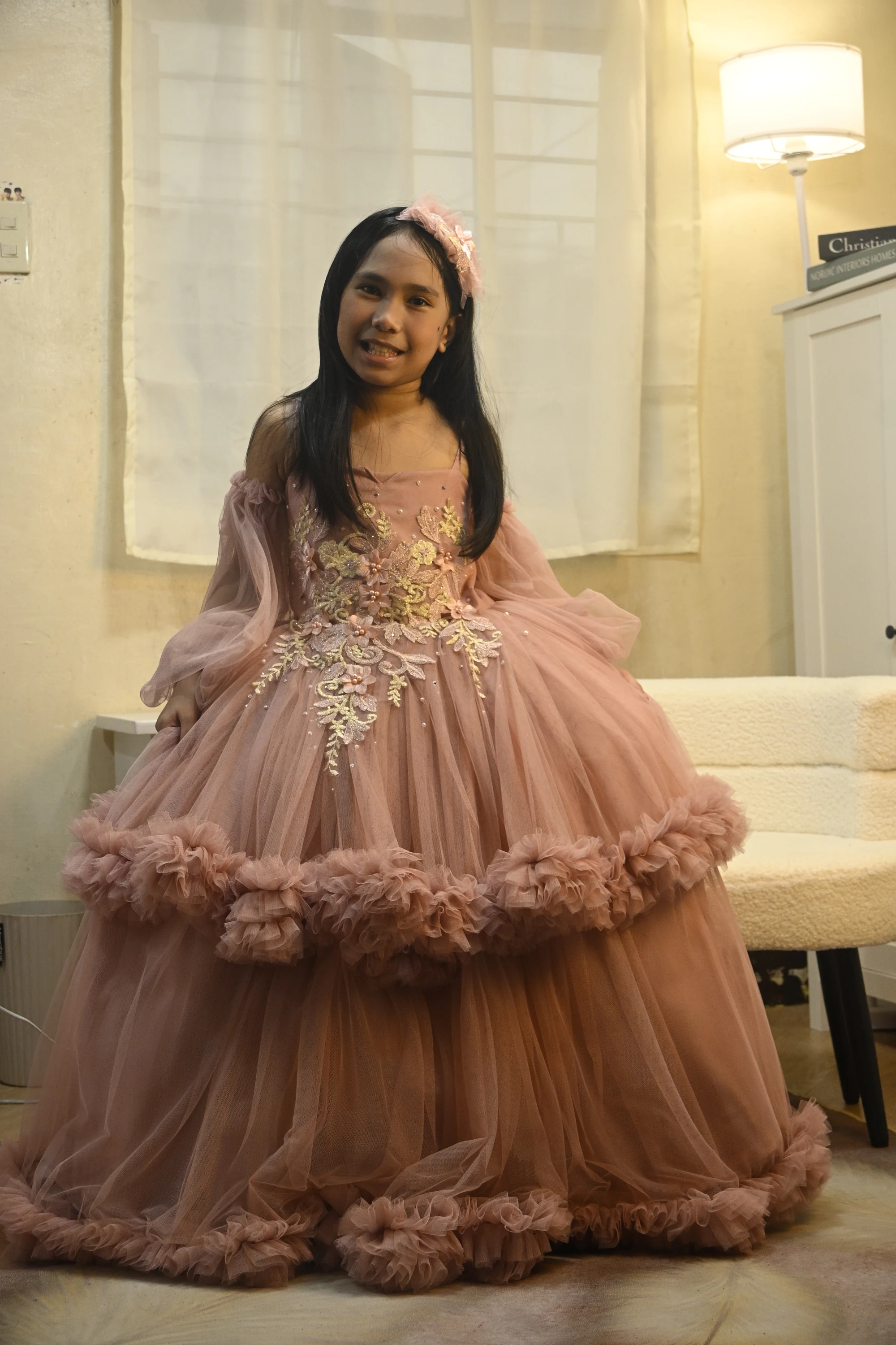 Full-length portrait of a model in a dusty-rose tulle gown with floral embroidery, sheer sleeves and tiered ruffles.