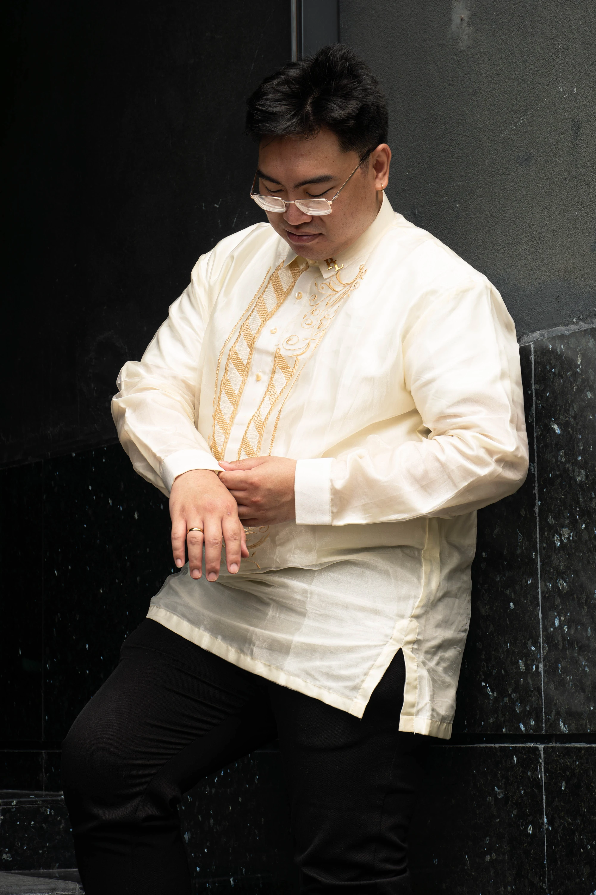 The groom looks down while adjusting the cuff of his embroidered barong.