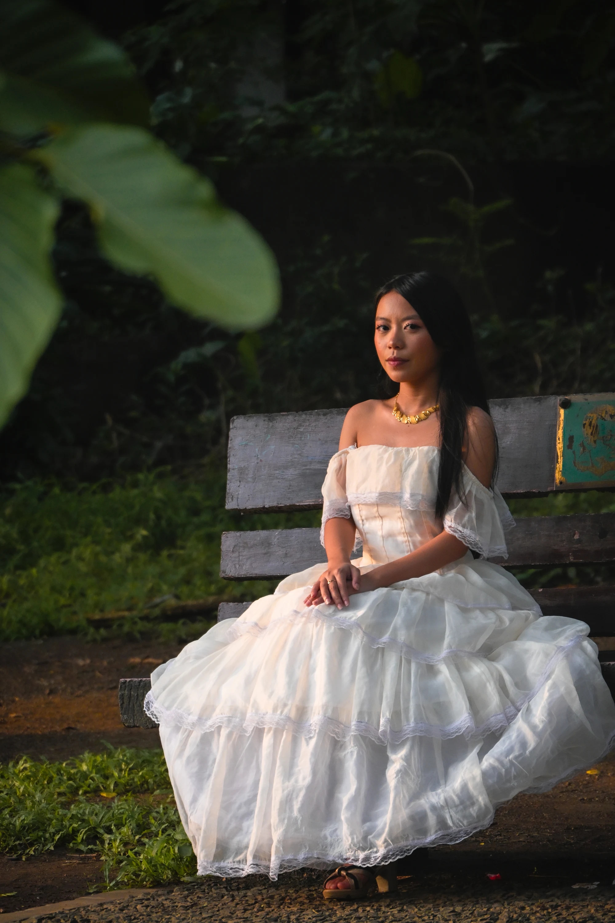 Seated portrait in a white gown on a wooden garden bench.