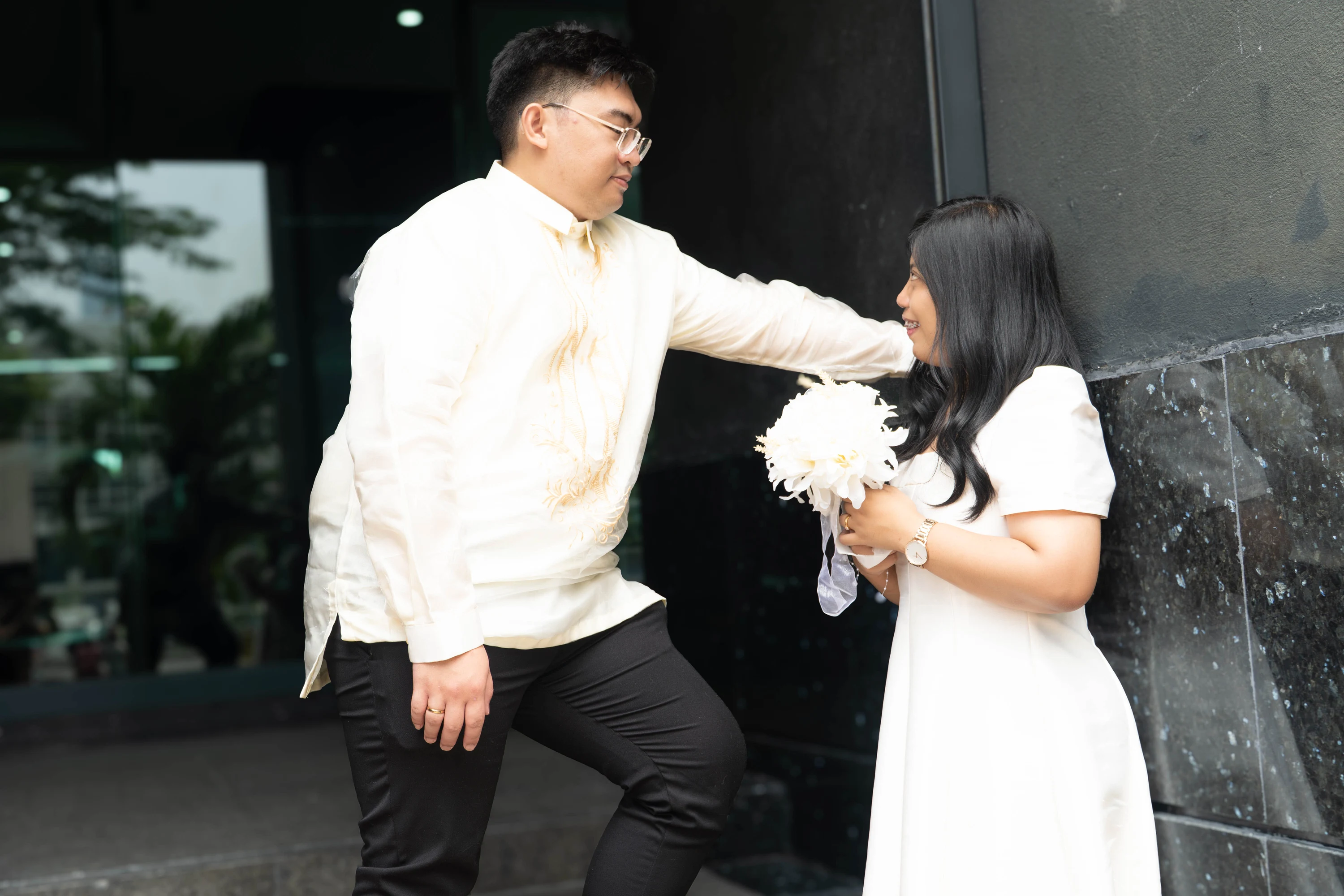 The couple faces one another beside the entrance steps, with the bride holding her bouquet.