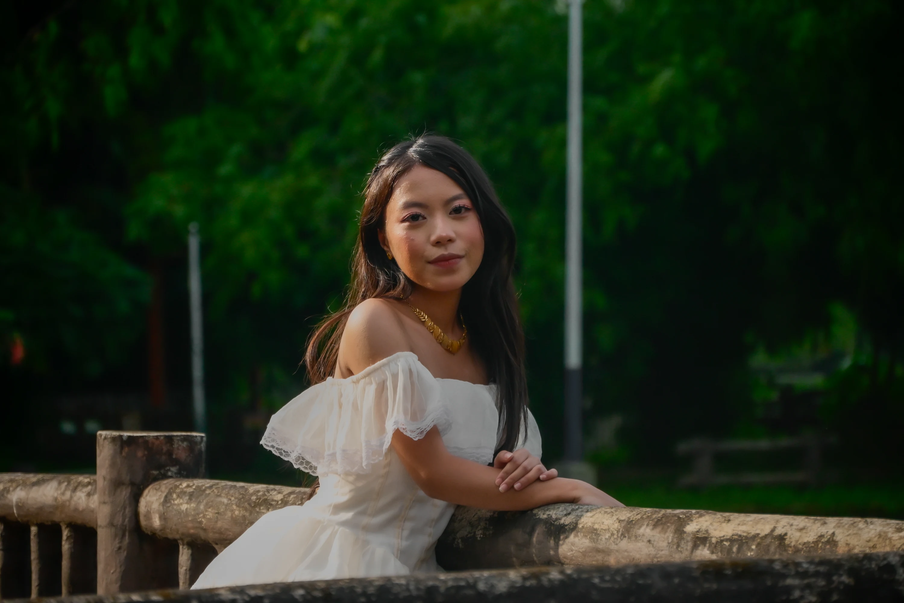Leaning on a wooden garden rail in a white gown, looking back toward the camera.
